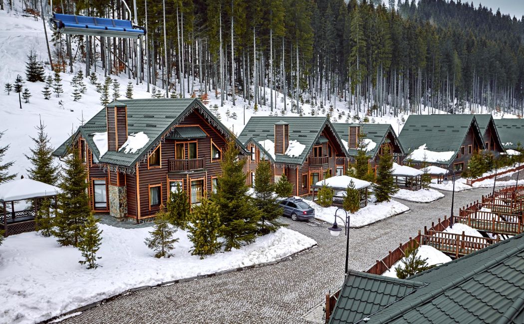 Custom log cabins with steep metal roofs and evergreen trees surrounded by deep winter snow in a Montana mountain setting