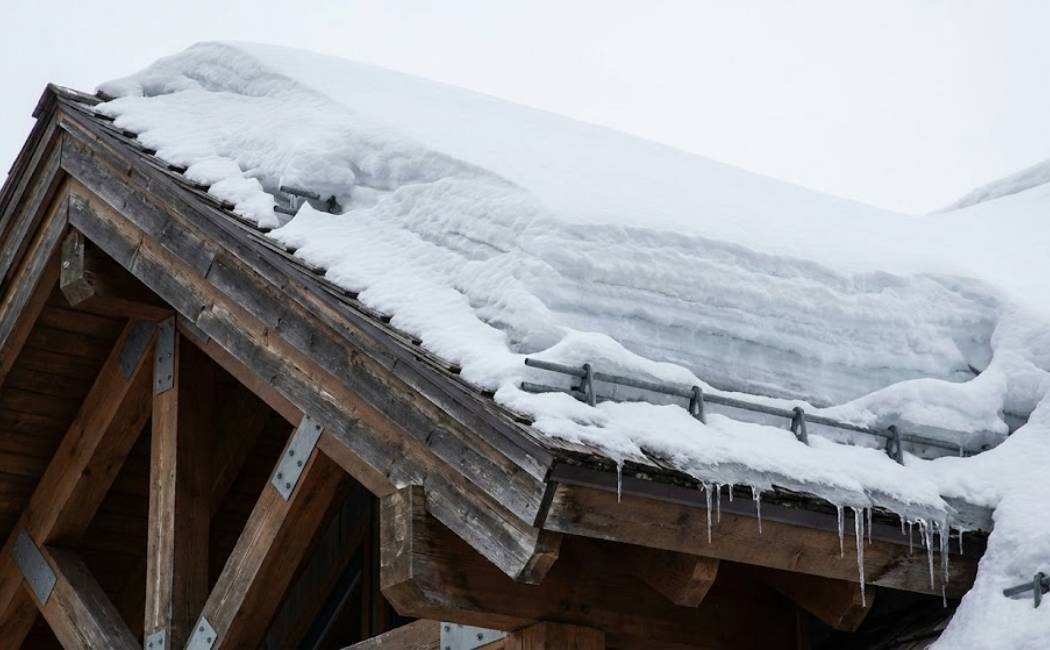 Close-up of a steep roof with compacted snow showing reinforced rafters and snow guards.