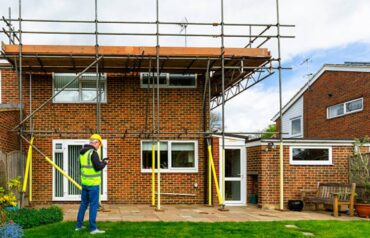 Construction worker inspecting scaffolding on a house undergoing renovation.