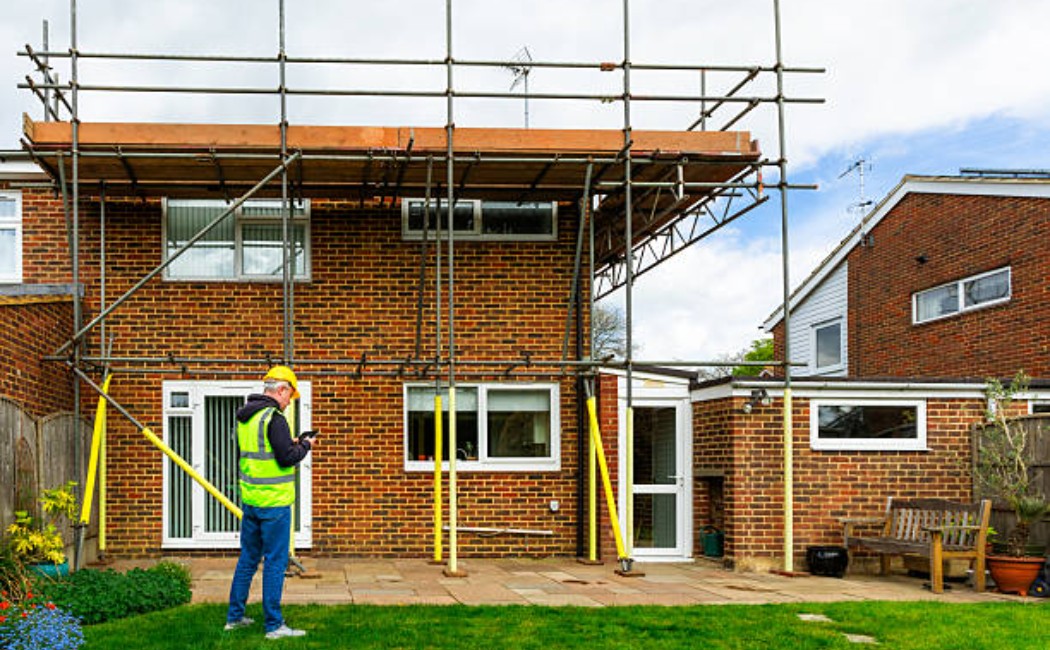 Construction worker inspecting scaffolding on a house undergoing renovation.