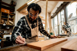 Skilled carpenter measuring timber in a woodworking workshop to ensure accurate custom carpentry work.