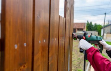 Worker building a custom wooden fence in a residential backyard